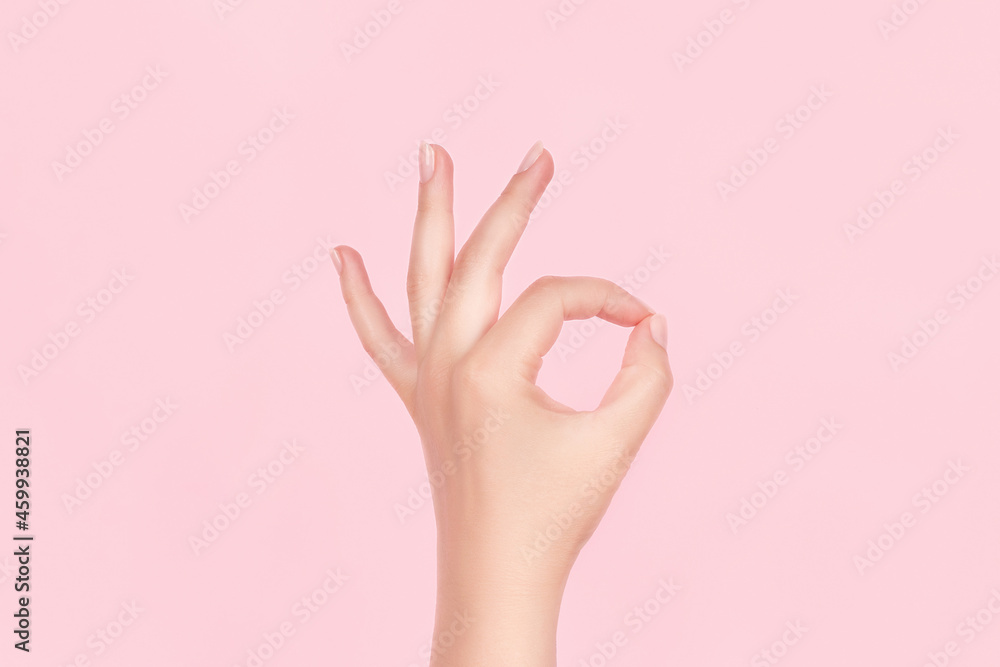 Female hand with beautiful manicure - pink nude nails making ok sign on pink background. Nail care concept