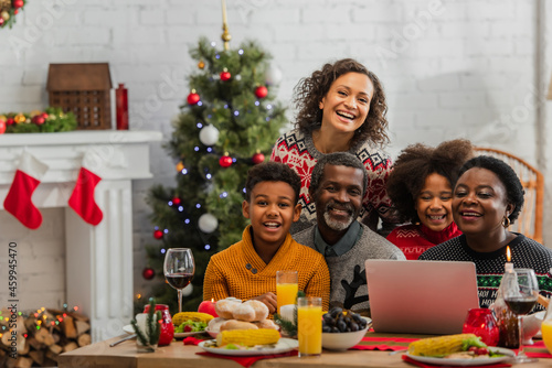 african american family smiling near laptop on table with christmas dinner