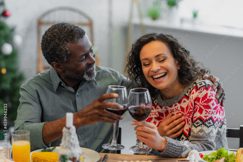 laughing african american woman clinking glasses of red wine with dad during christmas dinner