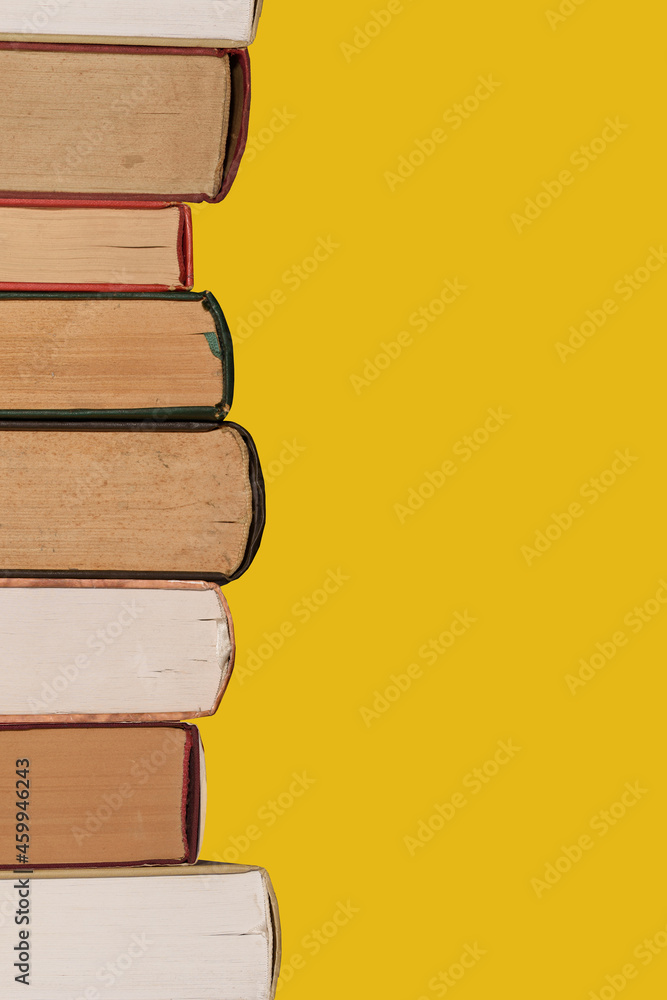 Stacked old books on the left. Isolated on a yellow background. Stacked old books on the left. Isolated on a yellow background.