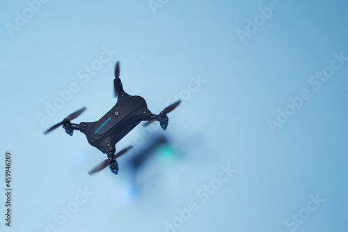 Aerial top down view on isolated drone copter with spinning propellers flying above the bright solid blue fond background