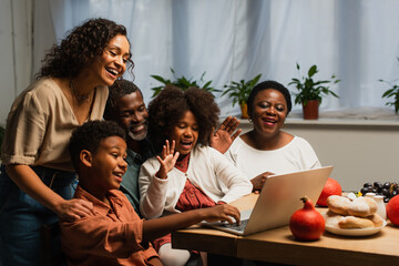 happy african american family waving hands during video call during thanksgiving dinner