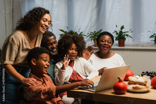 happy african american family waving hands during video call during thanksgiving dinner