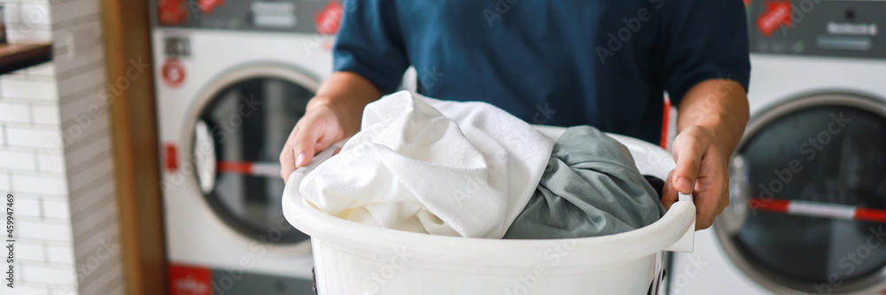 Man doing launder holding basket with dirty laundry of the washing machine in the public store. laundry clothes concept