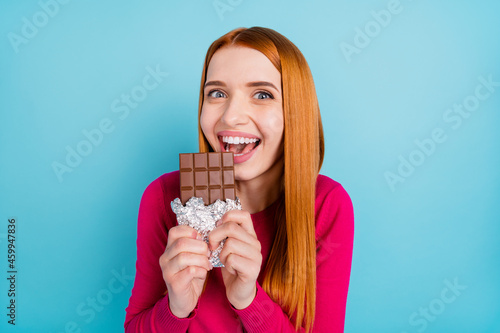 Photo of adorable funky young woman wear pink shirt biting milk dark chocolate smiling isolated blue color background