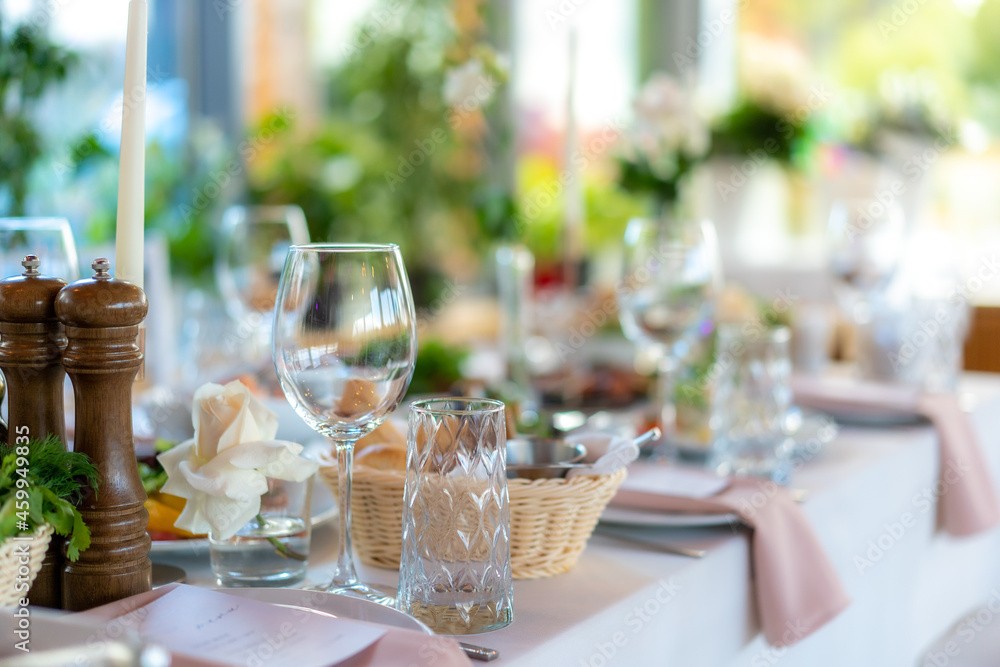 Fototapeta premium Wine glasses, flowers, fork, knife served for dinner in restaurant with cozy interior