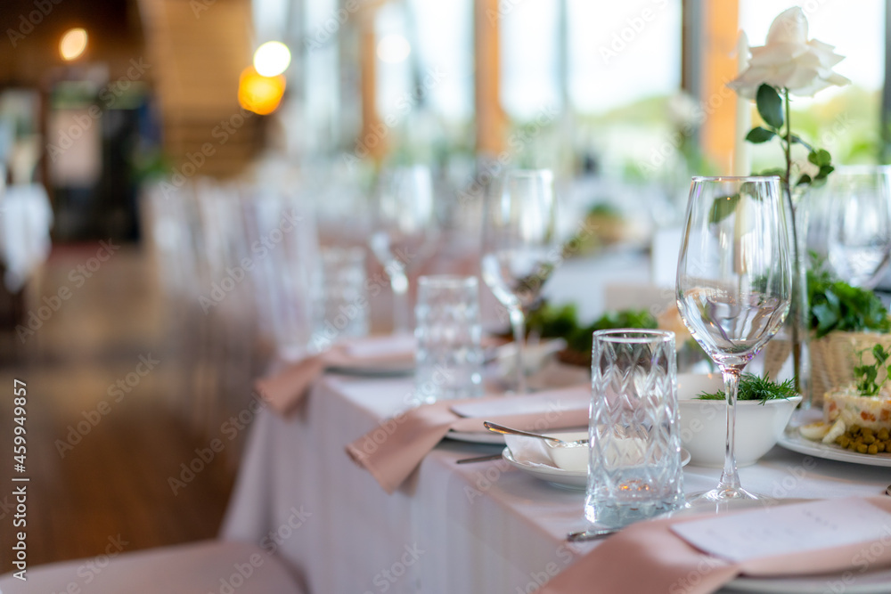 Wine glasses, flowers, fork, knife served for dinner in restaurant with cozy interior