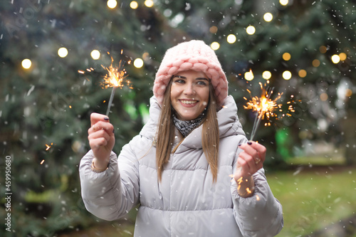 Cheerful lady having fun with sparklers at the street during the snowfall