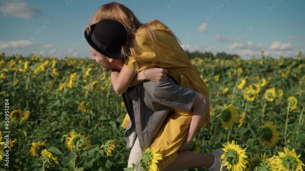 a couple of beautiful red-haired caucasian female in a long yellow dress in a sunflower field on a sunny day smiling, indulging, spinning, hugging with a nice guy in a black hat and shirt a couple of beautiful red-haired caucasian female in a long yellow dress in a sunflower field on a sunny day smiling, indulging, spinning, hugging with a nice guy in a black hat and shirt