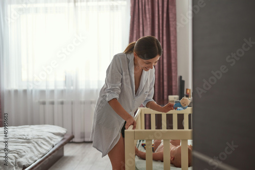 Woman entartaing baby in crib. Lifestyle portrait