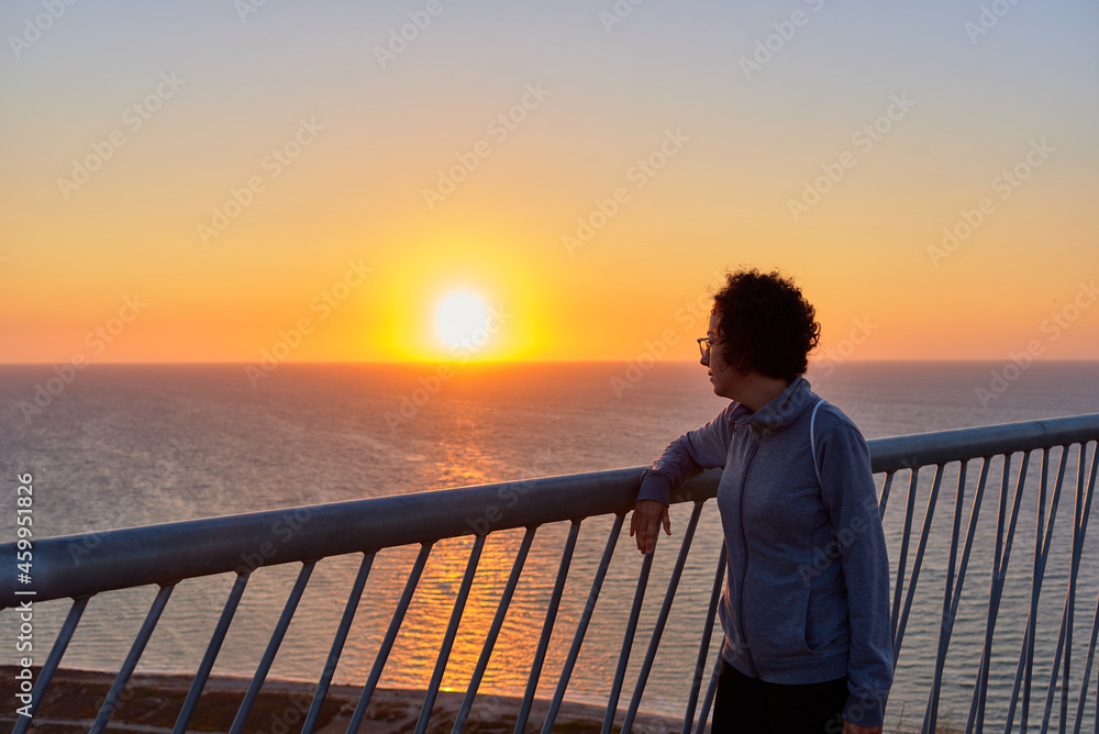 Woman looking at sunrise over the sea on a coast line