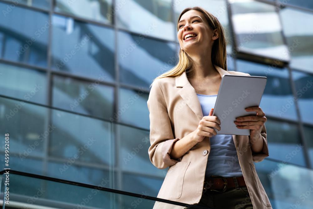 © NDABCREATIVITY - Portrait of a successful business woman using digital tablet in front of modern business building