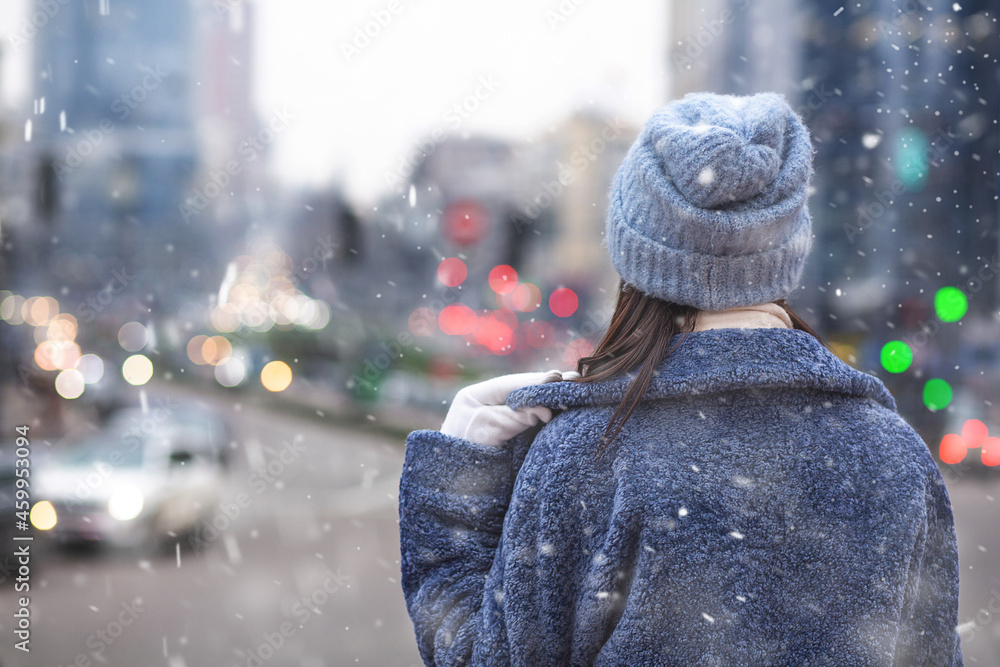 Woman wears coat and hat looking at the city in snowy weather Woman wears coat and hat looking at the city in snowy weather