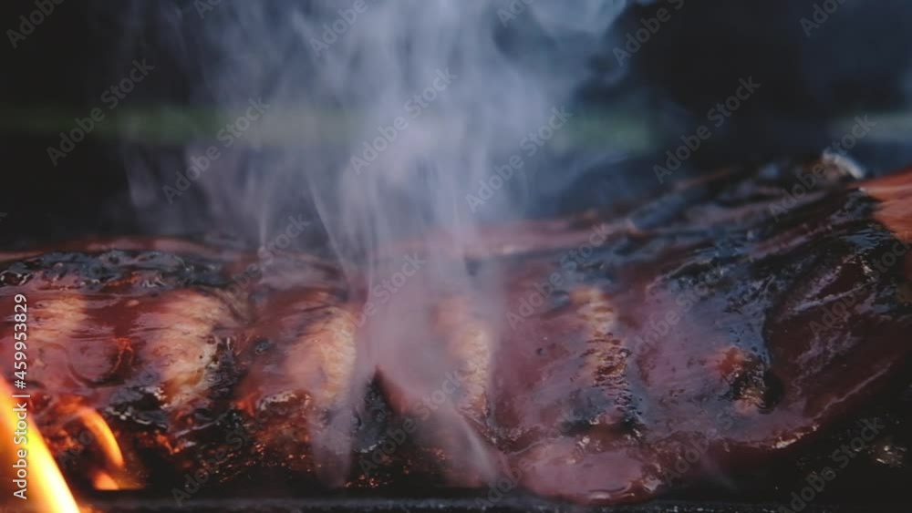 Barbecue picnic outside. Close-up of ribs fried on an open fire on grill in flame. steak poured with sweet BBQ sauce. cooking Delicious grilled meat in summer for large group of friends Barbecue picnic outside. Close-up of ribs fried on an open fire on grill in flame. steak poured with sweet BBQ sauce. cooking Delicious grilled meat in summer for large group of friends