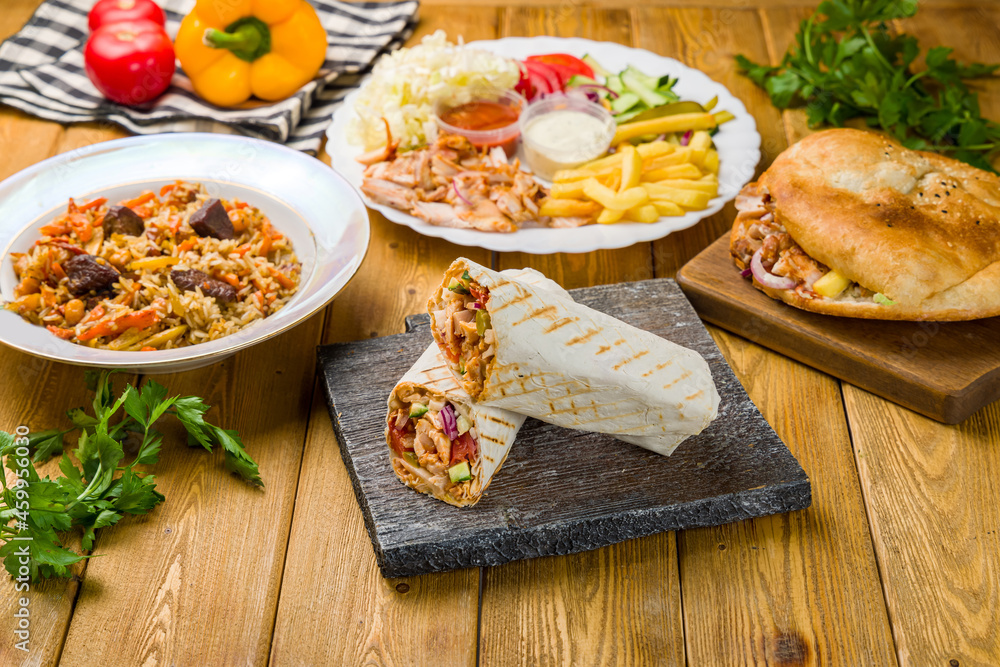 roll with chicken on the Board, pilaf with beef, pita with chicken and vegetables, chicken and vegetables on plate on wooden table roll with chicken on the Board, pilaf with beef, pita with chicken and vegetables, chicken and vegetables on plate on wooden table