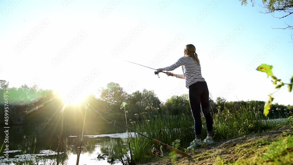 A young woman in a striped T-shirt, jeans and white croses catches fish on the banks of the river in the rays of the setting sun. Nature. Autumn. Fishing. Atmosphere. A young woman in a striped T-shirt, jeans and white croses catches fish on the banks of the river in the rays of the setting sun. Nature. Autumn. Fishing. Atmosphere.