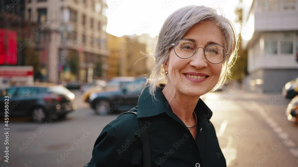 Close up portrait of a mature stylish business woman in the middle of a busy city street in the center. Portrait of an active aged woman near the business center. Slow motion Close up portrait of a mature stylish business woman in the middle of a busy city street in the center. Portrait of an active aged woman near the business center. Slow motion