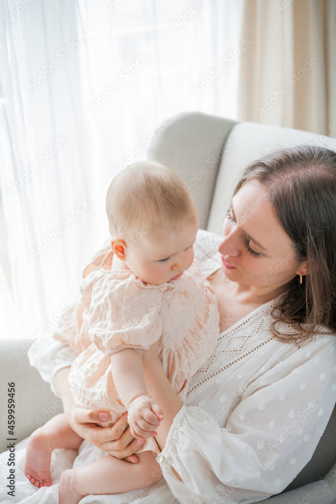 Happy young mother holds her little daughter 5 months old in her arms sitting in a chair at home. Motherhood. Happy young mother holds her little daughter 5 months old in her arms sitting in a chair at home. Motherhood.