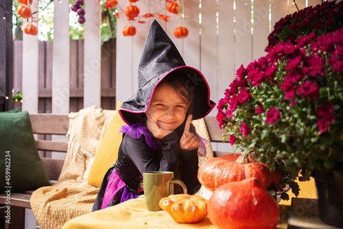 Funny little girl in a witch costume for Halloween looks out from behind a large tree Fotobehang
