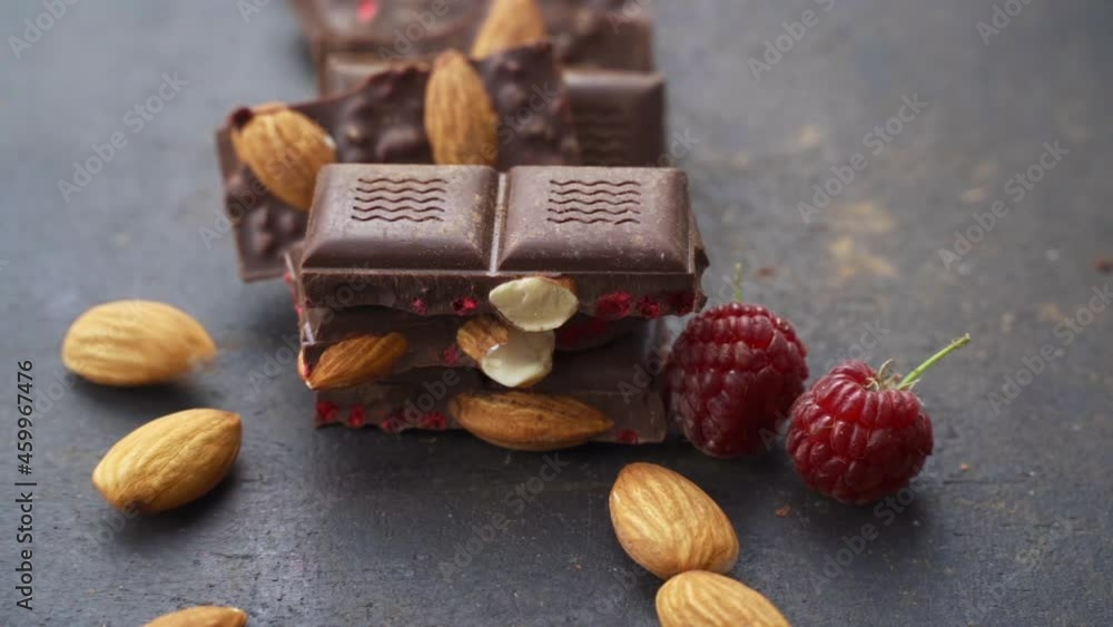 almond nuts falling on chocolate bar. Cooking chocolate bars with almonds, raspberries, handmade sweets. bars and pieces dark chocolate on black background. Confectionery craft on table almond nuts falling on chocolate bar. Cooking chocolate bars with almonds, raspberries, handmade sweets. bars and pieces dark chocolate on black background. Confectionery craft on table