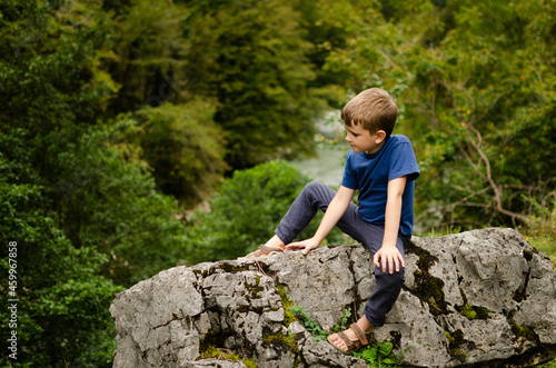 A boy sits on a large stone in nature