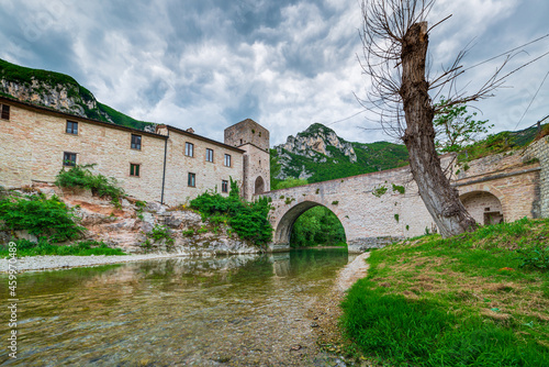 Dramatic sky over medieval village on river, San Vittore Frasassi, Marche, Italy. Romantic sky and clouds above mountains landscape, tourism destination. photo