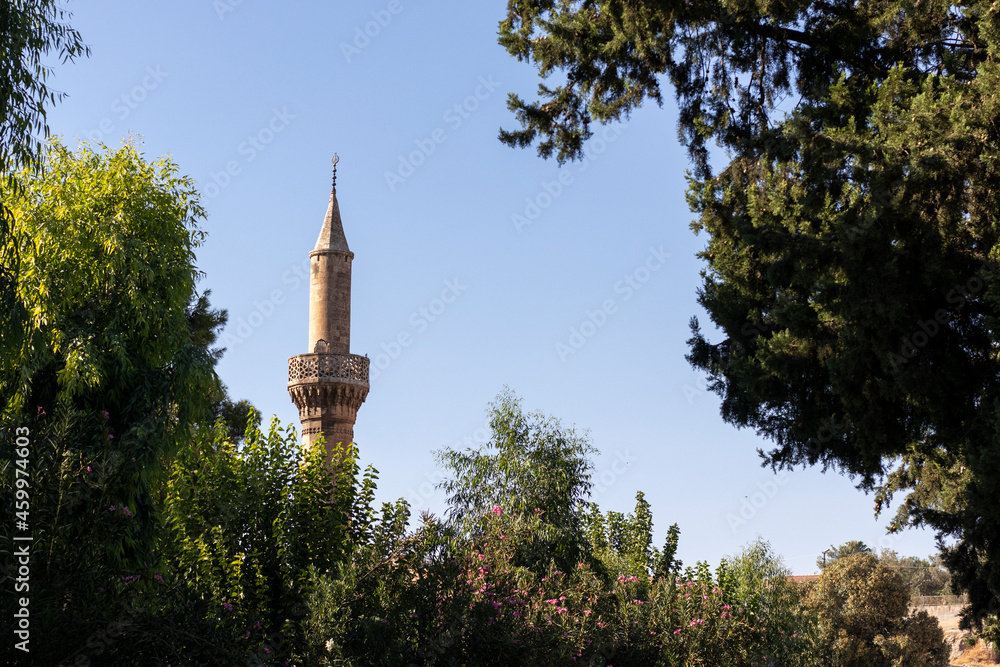 High minaret on a background of blue sky. View through the trees in a park. (Gaziantep, Turkey.)