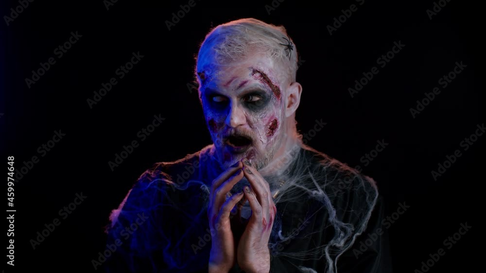 Frightening man with Halloween zombie bloody wounded face make-up, scared by police lights. Horror theme. Sinister undead guy isolated on studio black background. Voodoo rituals. Detention of criminal Frightening man with Halloween zombie bloody wounded face make-up, scared by police lights. Horror theme. Sinister undead guy isolated on studio black background. Voodoo rituals. Detention of criminal