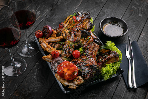 Assorted grilled meat with sauce and red wine on a black table. 