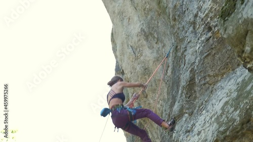 Young woman climber falling down after failed attemp to climb steep wall of rocky mountain. Engaging in extreme sport concept. photo