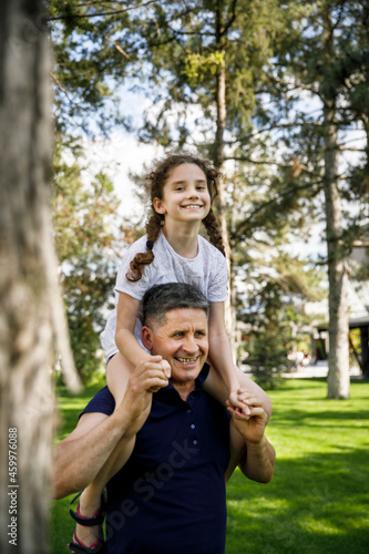 View of a grandfather holds his niece on his shoulders, he enjoys of a good day together in nature. Vertical view.