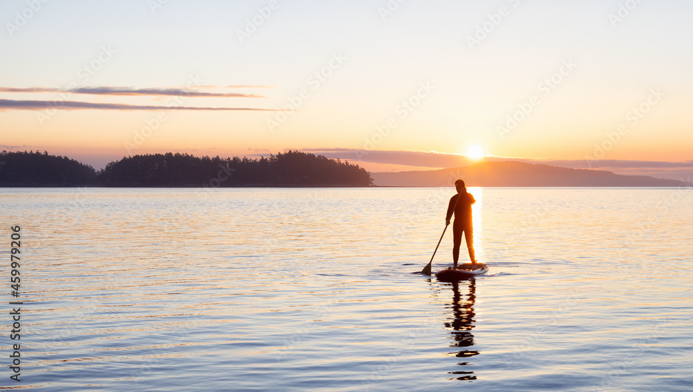 Adventurous Caucasian Adult Woman on a Stand Up Paddle Board is paddling on the West Coast of Pacific Ocean. Sunny Sunrise. Victoria, Vancouver Island, BC, Canada.