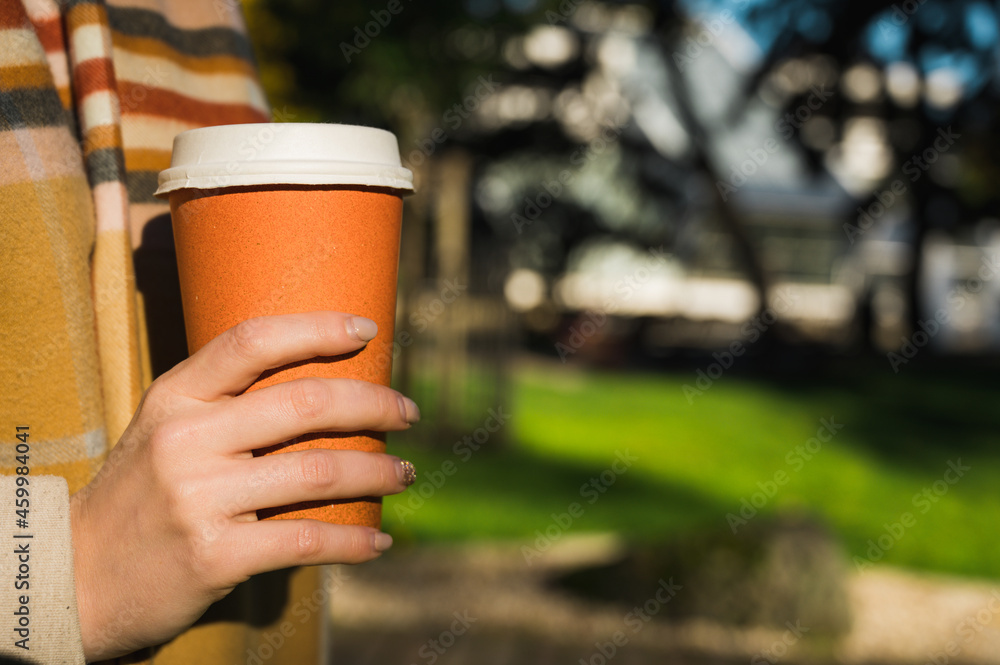 Close-up of orange cardboard cup of coffee in hand of woman. Take away drink. Warm scarf. Close-up of orange cardboard cup of coffee in hand of woman. Take away drink. Warm scarf.