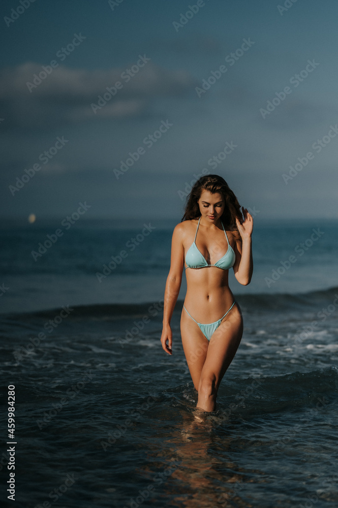 Fitness model girl posing in the sea in green color mini bikini.