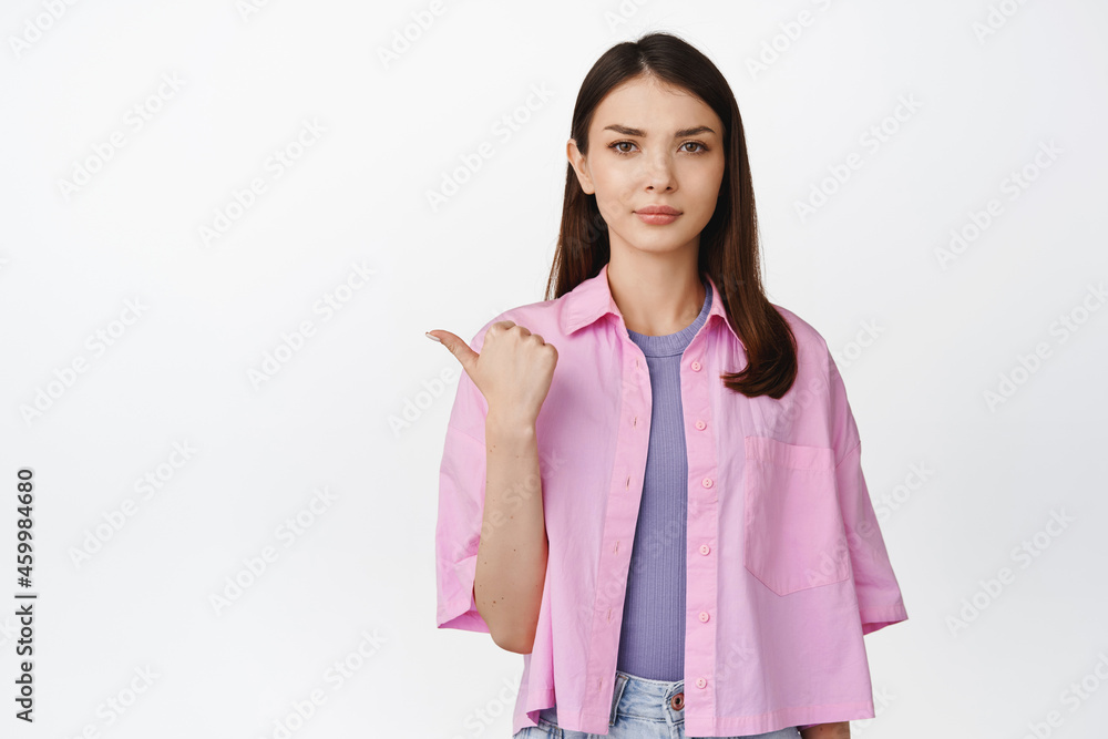 Angry brunette girl frowning, pointing finger left and looking disappointed, dislike something, standing over white background Angry brunette girl frowning, pointing finger left and looking disappointed, dislike something, standing over white background