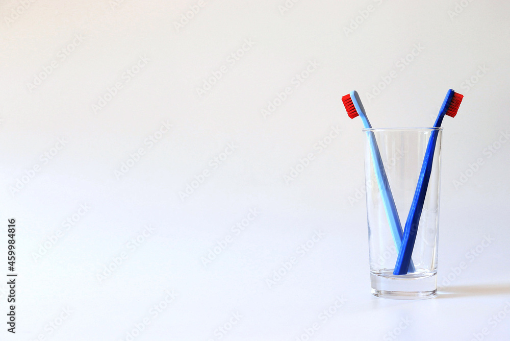 Dark blue and light blue toothbrushes in a glass on a white background Dark blue and light blue toothbrushes in a glass on a white background