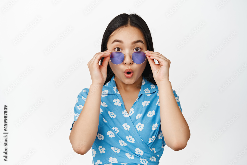 Image of brunette asian girl takes off sunglasses, looking surprised and intrigued by smth cool, checking out advertisement, white background Image of brunette asian girl takes off sunglasses, looking surprised and intrigued by smth cool, checking out advertisement, white background
