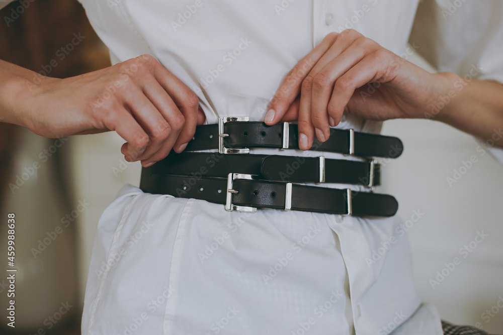 Young girl in a white office shirt trying on a leather belt