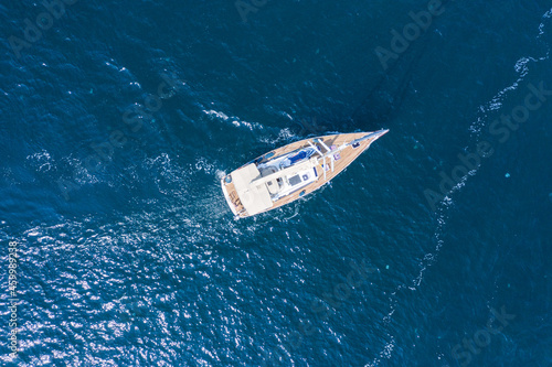 Aerial view of a beautiful white sailing yacht with a colored sail.