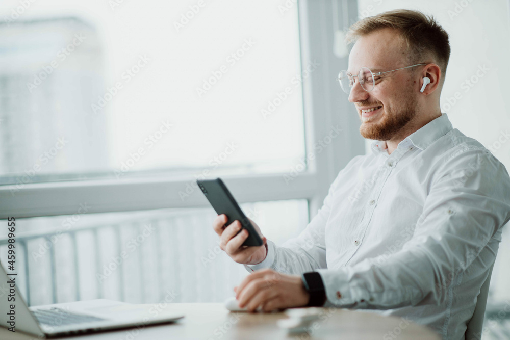 man in wireless headphones communicates on a smartphone videoconference in a bright room. man in wireless headphones communicates on a smartphone videoconference in a bright room.