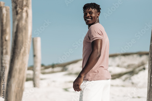 Handsome african man , smiling and looking at camera while walking in sandy desert against blue sky