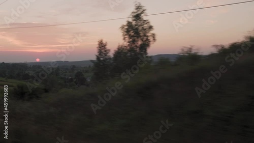 view from window high-speed train on landscape of nature field and forest on evening dusk sky sunset in summer background. red setting sun on horizon. Transport, travel, railway, communication concept