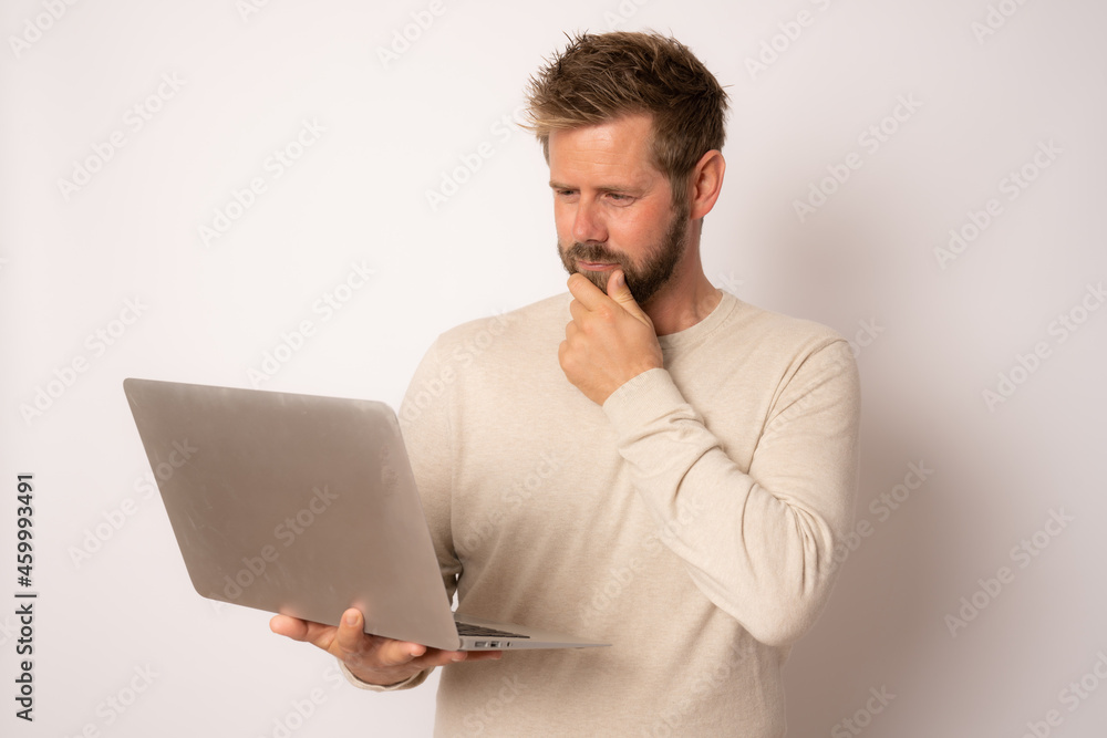 Studio portrait of a young pensive man in a casual sweater with a laptop on a white background Studio portrait of a young pensive man in a casual sweater with a laptop on a white background
