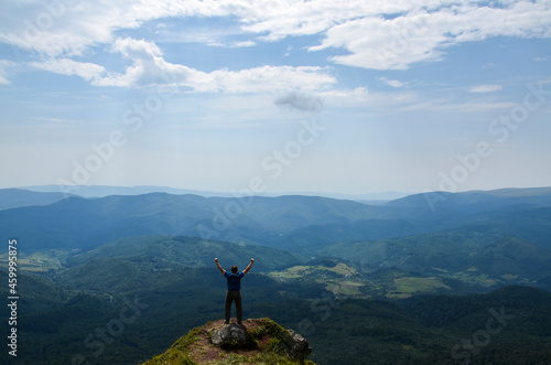 Back view of man hiker standing on the rock in the beautiful mountains with rising hands and enjoying amazing landscape, summer time. Carpathian Mountains, Ukraine