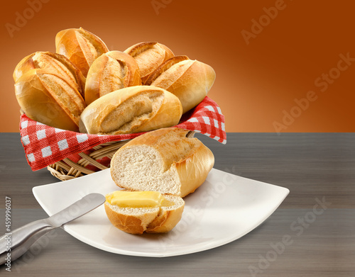 Cesta de pães com toalha xadrez e prato com pão e manteiga em fundo de mesa.  photo