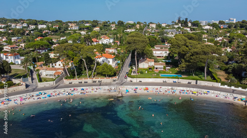 Aerial view of expensive estates behind Ondes Beach on the Cap d'Antibes in the French Riviera - Tourists sunbathing by the Mediterranean Sea in the South of France