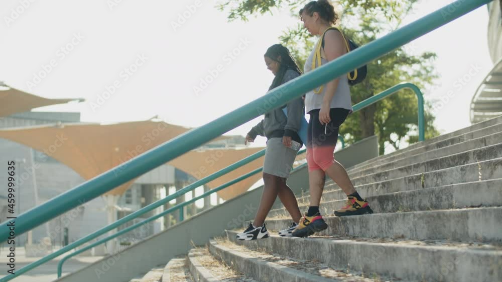Long shot of fat women going down stairs of sports complex. Tracking shot of diverse female friends going home after workout in gym, talking, discussing trainings. Obesity, sport concept Long shot of fat women going down stairs of sports complex. Tracking shot of diverse female friends going home after workout in gym, talking, discussing trainings. Obesity, sport concept