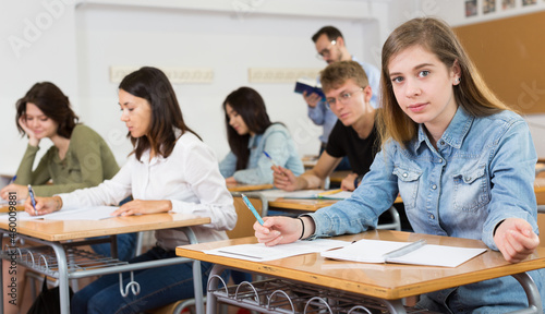 Smiling schoolgirl is learning and answering the question on paper in the class.