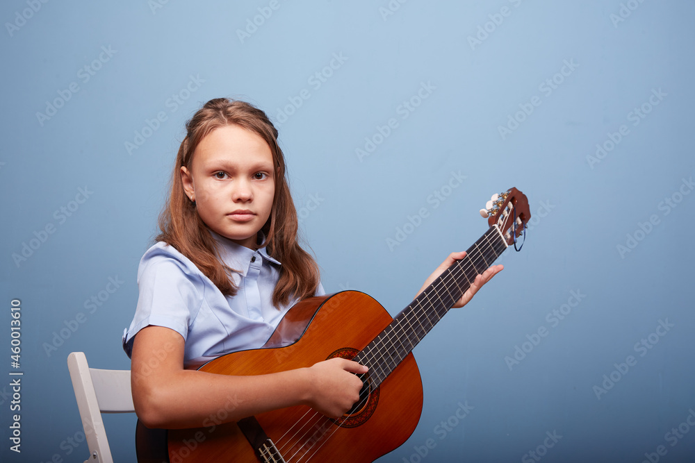 Fototapeta premium an 11-year-old girl is practicing a melody on a guitar on a blue background