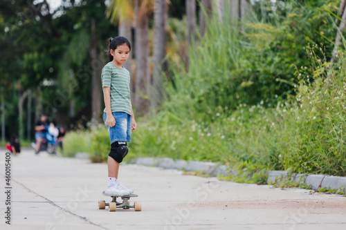 Asian child girl learning to skateboard outdoors. Kid having fun and playing skateboard on the road at the day time. Kid activity and extreme sport concept.